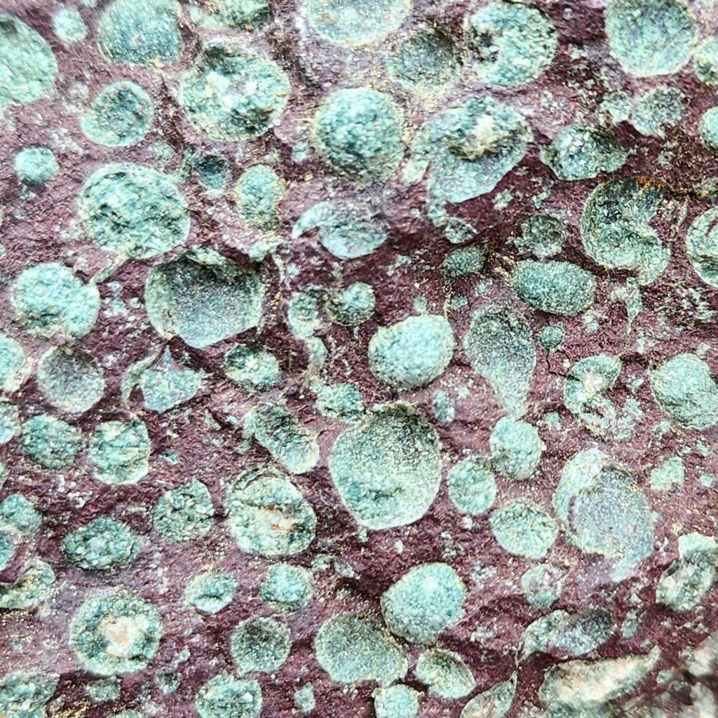 close up of green solid filled bubbles in brownish-red rock